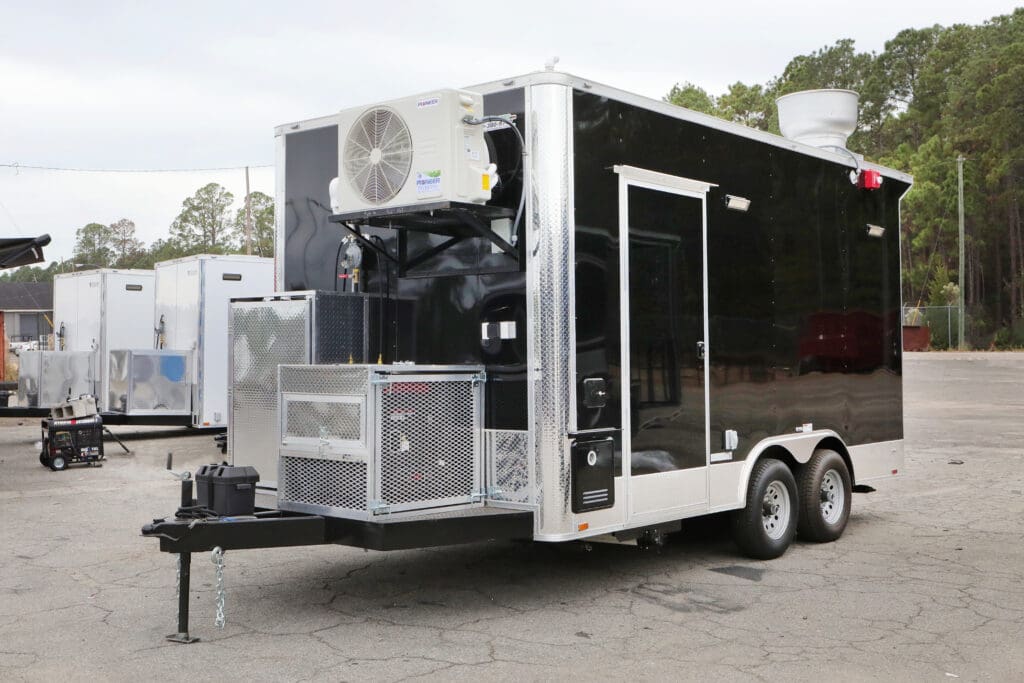 8.5 x 24' Freedom BBQ Food Concession Trailer, black with white trim, featuring an exterior-mounted air conditioning unit and other equipment, parked on asphalt with other trailers in the background